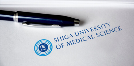 写真:滋賀医科大学のロゴの紙の上にペンを置いている